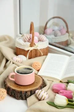 Easter decorations. Cup of coffee, painted eggs, tulips and book on windowsil Stock Photos