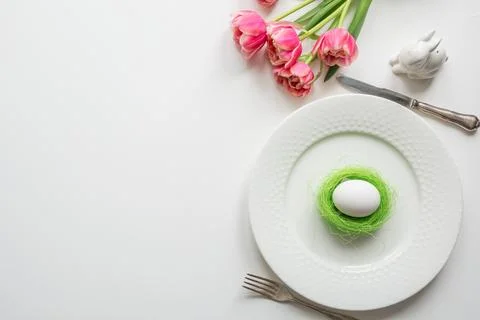 Easter dinner. Table setting with pink tulip, eggs on white table. Top view. Stock Photos