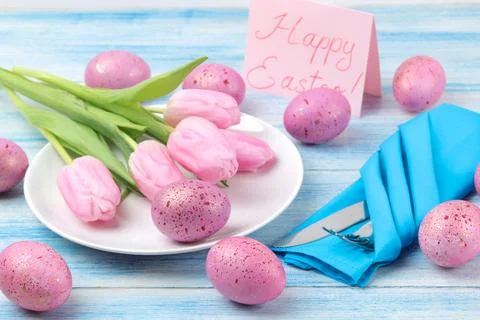 Easter. Easter table setting. Pink easter eggs and flowers tulips on a blue w Stock Photos
