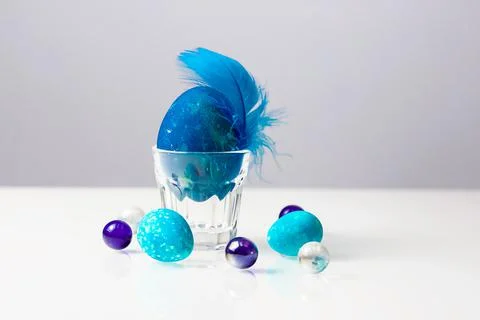 Easter egg with blue feather in transparent egg holder on white table Stock Photos