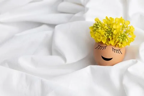 Easter egg with cute face and wreath of yellow flowers on white fabric Stock Photos
