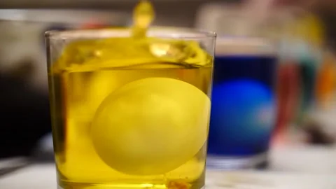 Easter egg falling into glasses of yellow dye in slow motion Stock Footage 151503348
