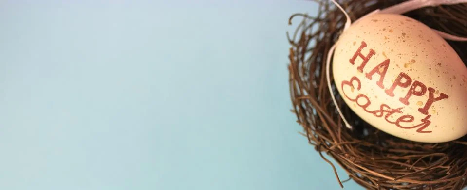 Easter egg with Happy Easter inscribed in bird's nest on pastel blue backgrou Foto stock