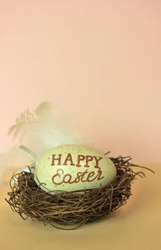 Easter egg with Happy Easter inscribed in a nest, white feather, nude background Foto stock