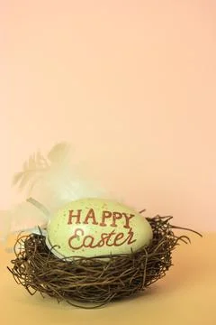 Easter egg with Happy Easter inscribed in a nest on warm nude background. Stock Photos