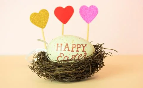 Easter egg with Happy Easter inscribed in a nest, multicolored hearts, a feat Stock Photos