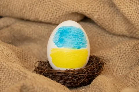 Easter egg with the image of the flag of Ukraine in a nest on a burlap backgr Stock Photos