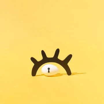 Easter egg with keyhole under black wooden eyelash against yellow background Stock Photos