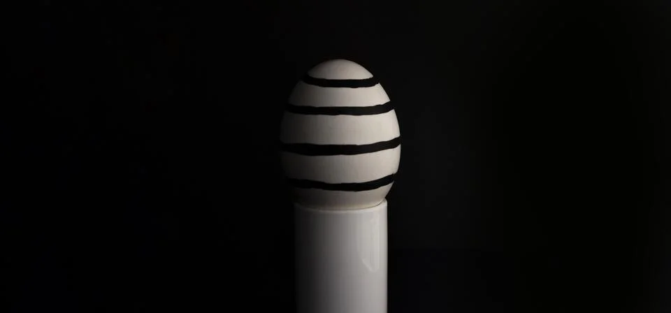 Easter egg with a minimalistic striped pattern on a stand on a black background. Stock Photos