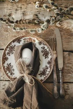 Easter egg in napkin, feather, setting with vintage plate, cutlery, willow .. Stock Photos
