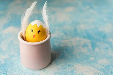 Easter egg painted as chick with funny face in the pink cup on blue background Stock Photos