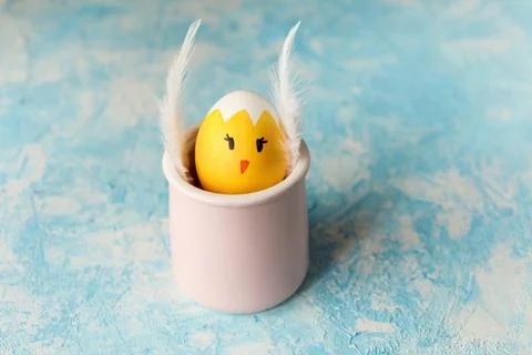 Easter egg painted as chick with funny face in the pink cup on blue background Stock Photos