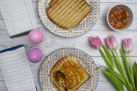 Easter egg in plate on a breakfast table with jam and pink white tulips. Stock Photos