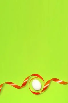Easter egg with a red ribbon on a green plain background. Space for text. Ver Stock Photos