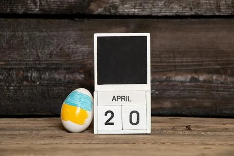 Easter egg with Ukrainian flag next to calendar with date April 20 on woode.. Stock Photos