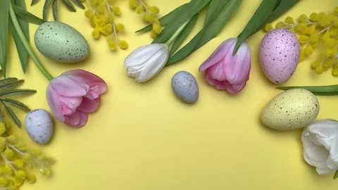Easter eggs and spring flowers creating festive border on yellow background Video stock 305531554