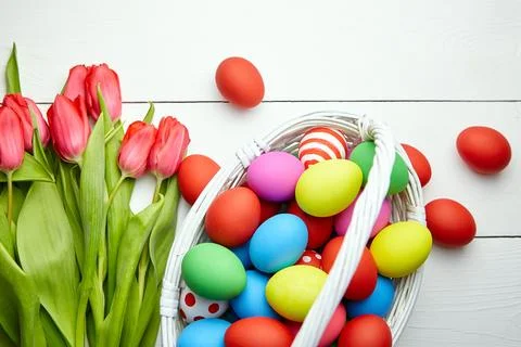 Easter Eggs in basket and spring flowers on white wooden table Stock Photos