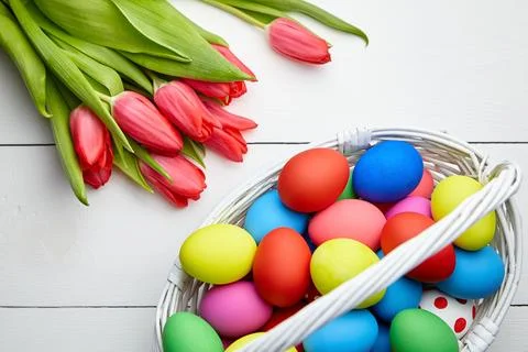 Easter Eggs in basket and spring flowers on white wooden table Stock Photos
