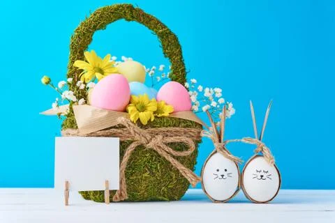 Easter eggs in basket with empty paper sheet on a blue background Stock Photos