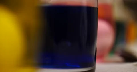 Easter eggs being lifted out of glass full of blue dye close up Stock Footage 151504153