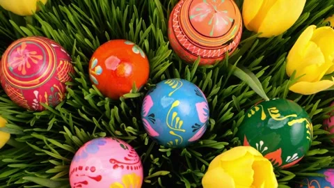 Easter eggs in bold, hand-painted designs lie among green grass and tulips... Stock Footage 299239855