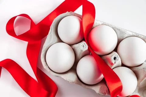 Easter eggs in a cardboard box with a red festive ribbon on a white backgroun Stock Photos
