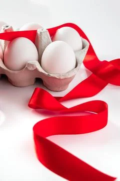 Easter eggs in a cardboard box with a red festive ribbon on a white backgroun Stock Photos