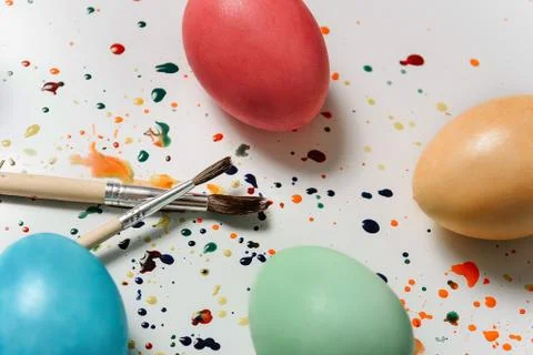 Easter eggs close-up on a smeared white paint surface next to paint brushes. Foto stock