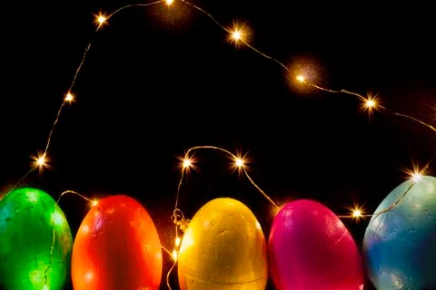 Easter eggs of different colors on a black background and lights. Stock Photos
