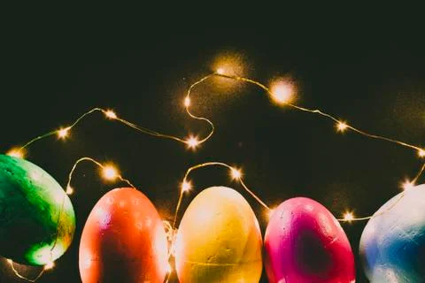 Easter eggs of different colors on a black background and lights. Stock Photos