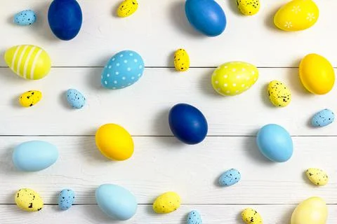 Easter eggs of different sizes, yellow and blue, lie on a white wooden table in 스톡 사진