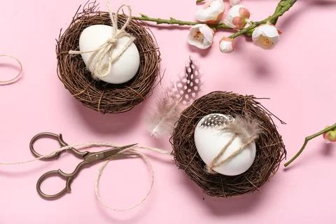 Easter eggs with feathers, rope, scissors and cherry blossom branch on pink b Stock Photos
