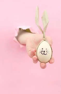 Easter eggs in the form of a rabbit in a female hand on a pink background Stock Photos