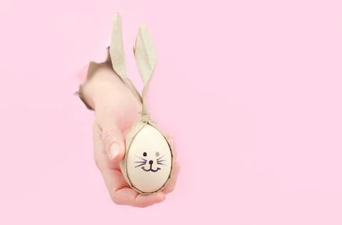 Easter eggs in the form of a rabbit in a female hand on a pink background Stock Photos