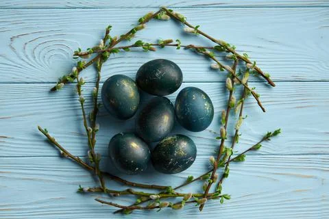 Easter eggs in a frame of branches on a blue wooden background. Minimalistic Stock Photos