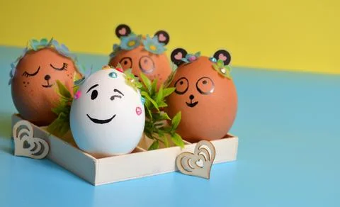 Easter eggs with funny faces in a box on a yellow-blue background. Easter. Stock Photos