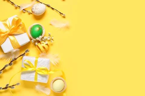 Easter eggs with gift boxes, flowers and pussy willow branches on yellow back Stock Photos