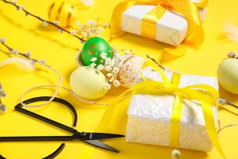 Easter eggs with gift boxes, rope, flowers and pussy willow branches on yello Stock Photos