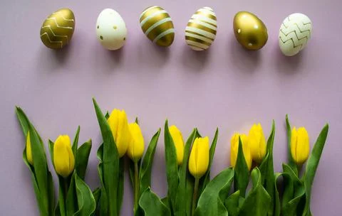 Easter eggs of gold, white  with pattern, yellow tulips on lilac background Stock Photos
