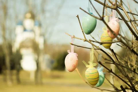 Easter eggs hang on tree branches against the backdrop of the church. Stock Photos