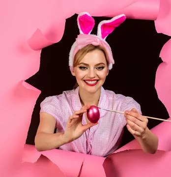 Easter eggs ideas. Smiling Rabbit girl painting egg. Happy woman in bunny ear Stock Photos