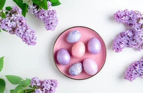 Easter eggs lie on a plate framed by flowering branches of lilac Stock Photos