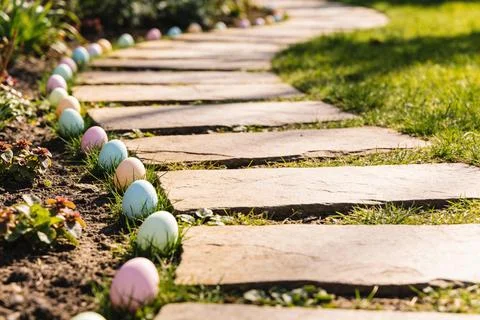 Easter eggs line a garden path with stepping stones and green grass on a su.. 스톡 사진