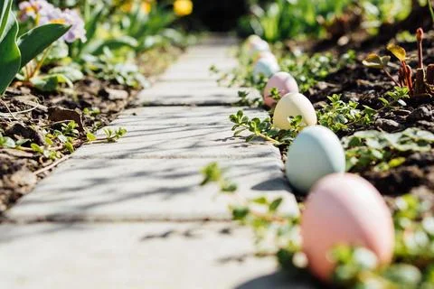 Easter eggs lined up on a garden path with blooming flowers and green foliage Stock Photos
