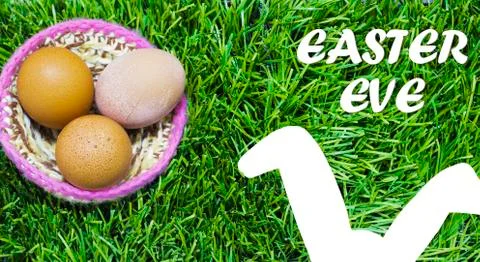 Easter eggs in nest on grass with text: Easter eve. Stock Photos