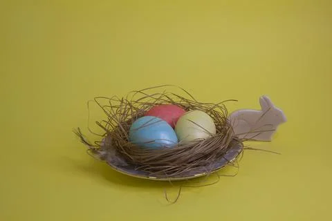 Easter eggs in the nest on yellow background. Greeting card. Stock Photos