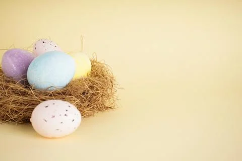 Easter eggs in a nest on a yellow background, space for text. Stock Photos