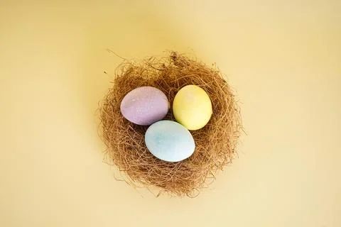 Easter eggs in a nest on a yellow background, flat lay. Stock Photos