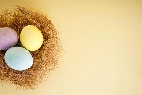Easter eggs in a nest on a yellow background, space for text. Top view. Stock Photos