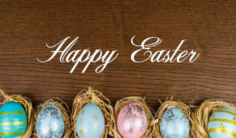 Easter eggs nested in straw on a wooden table with Happy Easter caption Stock Photos